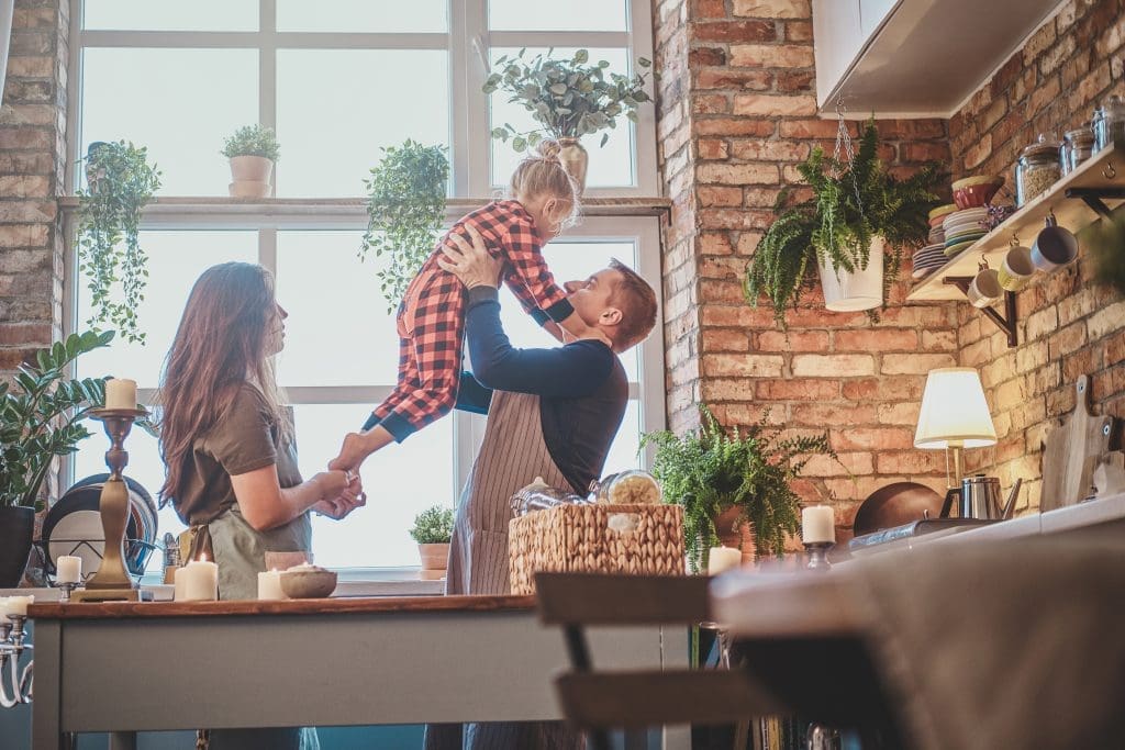 Mother and father holding 6-year old daughter in their brightly-lit kitchen of their new lease to own home in Raleigh, NC