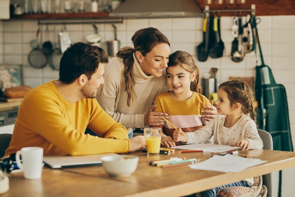 Mother and father with two young daughters smiling at the dining table of their new lease to own home in Raleigh, NC