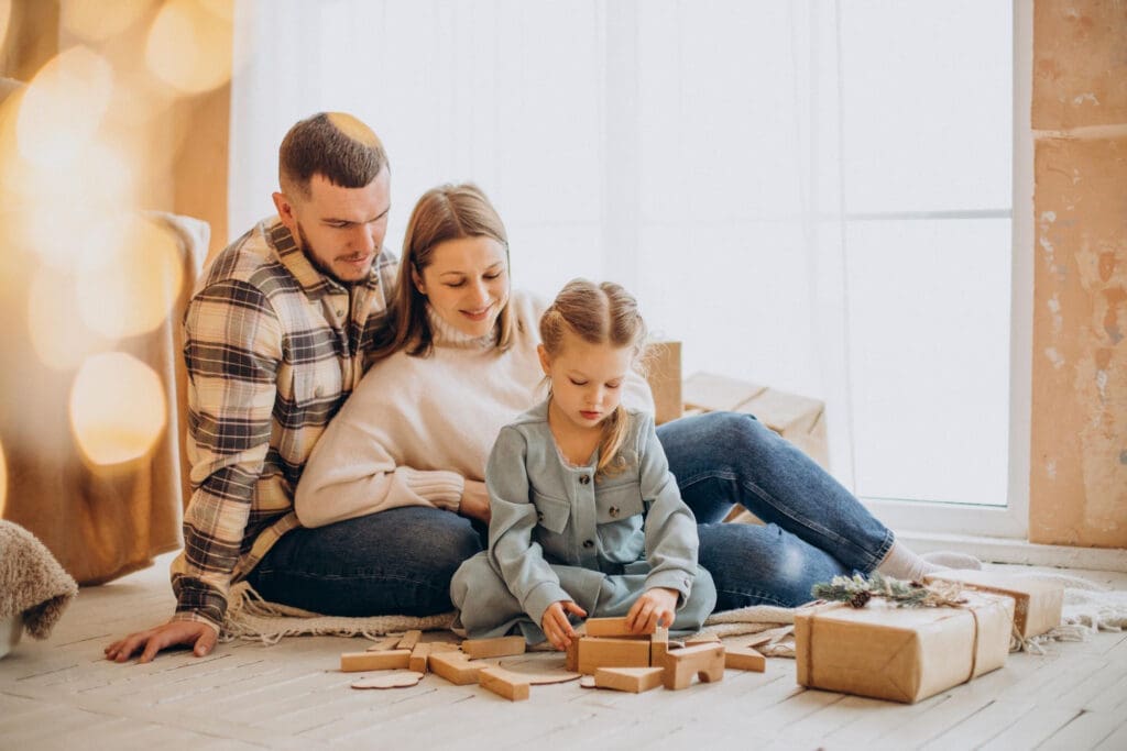 A happy family enjoying quality time together, as a couple watches their daughter play with wooden blocks. The lease to own program provides them a stable and comfortable lease to own home in Raleigh, creating the perfect space for making cherished family memories.