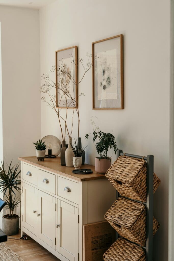 A stylish corner table in a lease-to-own home in Raleigh NC, decorated with mini vases on top, framed artwork hanging on the wall, and aesthetic wooden bins on the side, creating a warm and inviting space.