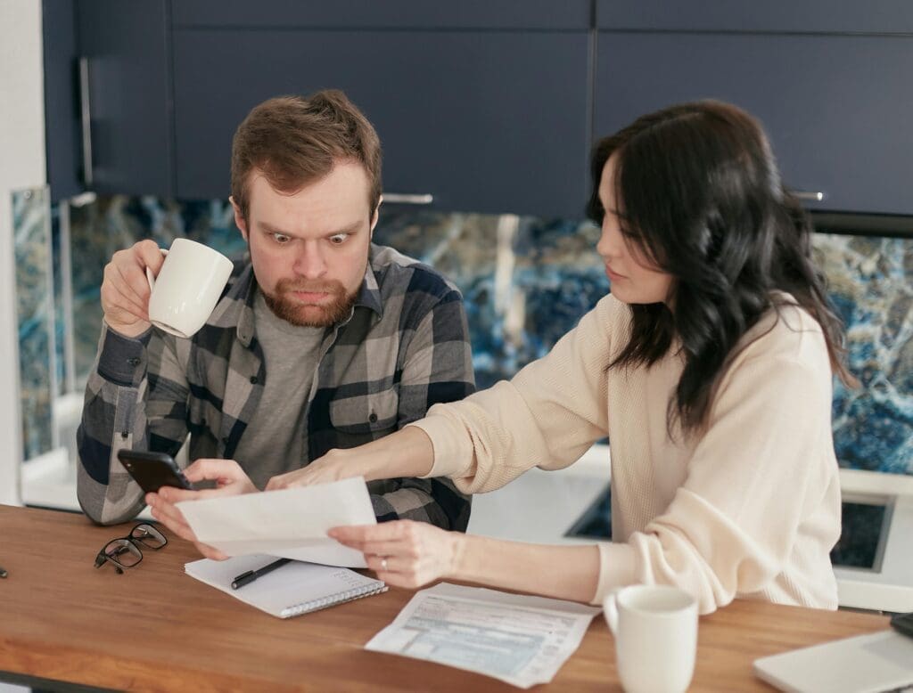 Couple at kitchen table reviewing homeownership documents, expressing the stress of potentially selling at a loss and exploring Lease-to-Own Raleigh options