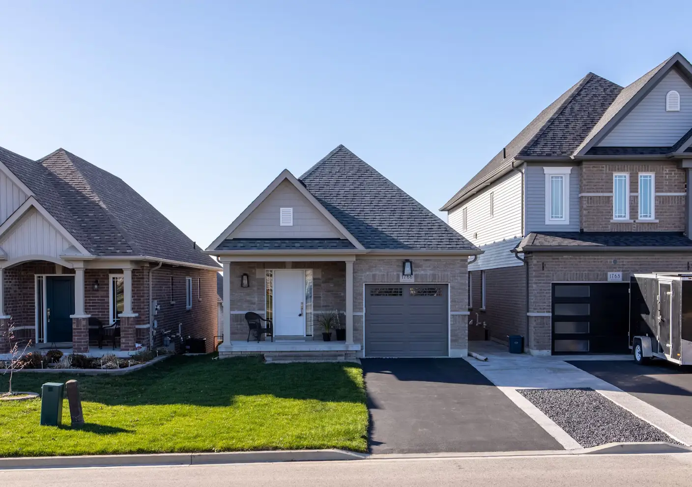 A small, modern grey brick house with a white front door, located in a residential subdivision under a clear blue sky in a lease to own Greensboro home.
